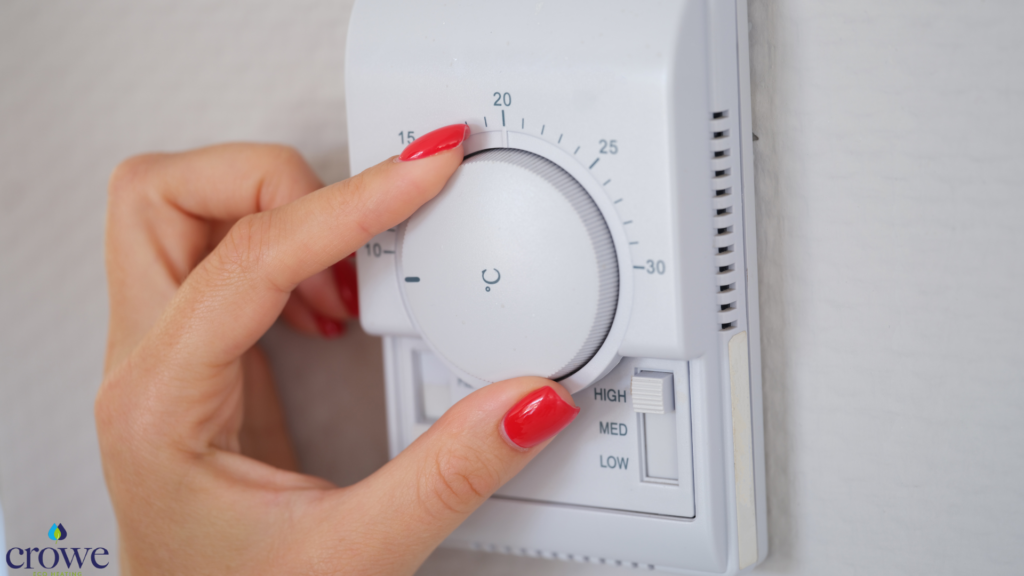 A manual thermostat on a wall. A female hand with orange finger nails is turning the dial